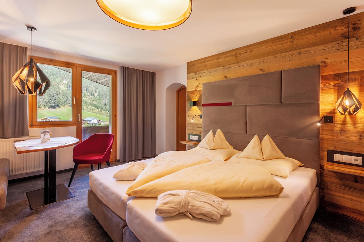 Ein Hotelzimmer mit einem großen Bett, einem Schreibtisch, einem roten Sessel und Blick ins Freie.