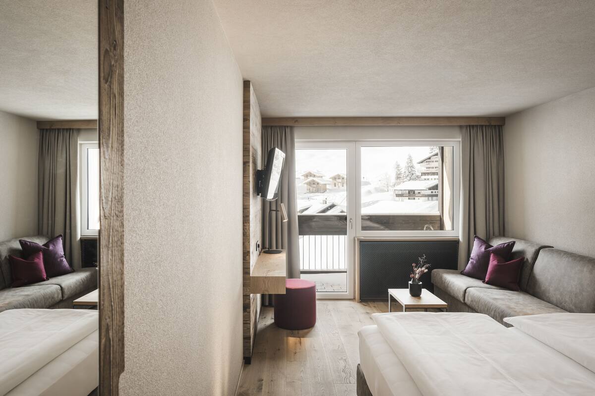 Ein Hotelzimmer mit zwei Betten, einem Schreibtisch, einem Fernseher und Blick auf eine verschneite Landschaft.