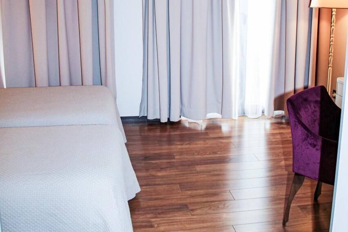 A hotel room with a large bed, wooden flooring, and a purple chair.