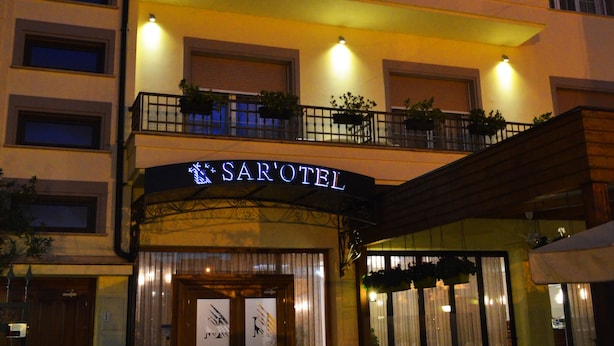 Un hotel de varios pisos con balcones, mobiliario exterior y una entrada bien visible.