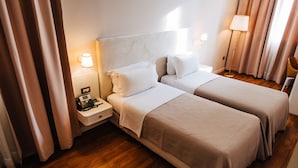Habitación de hotel con dos camas, una mesita de noche con teléfono, una lámpara y una silla.