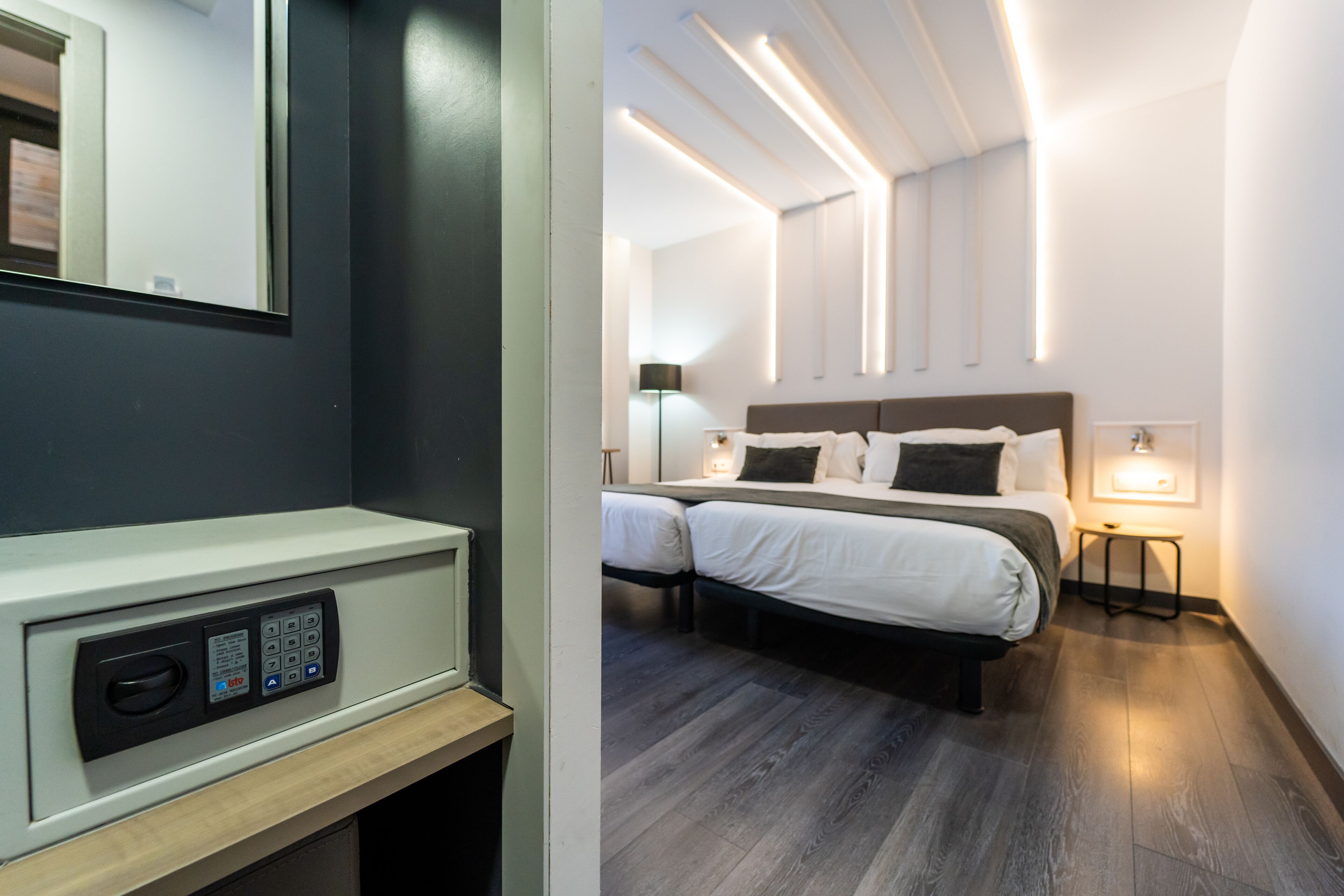 A modern hotel room with a control panel, a double bed, bedside tables, and a wall-mounted light fixture.