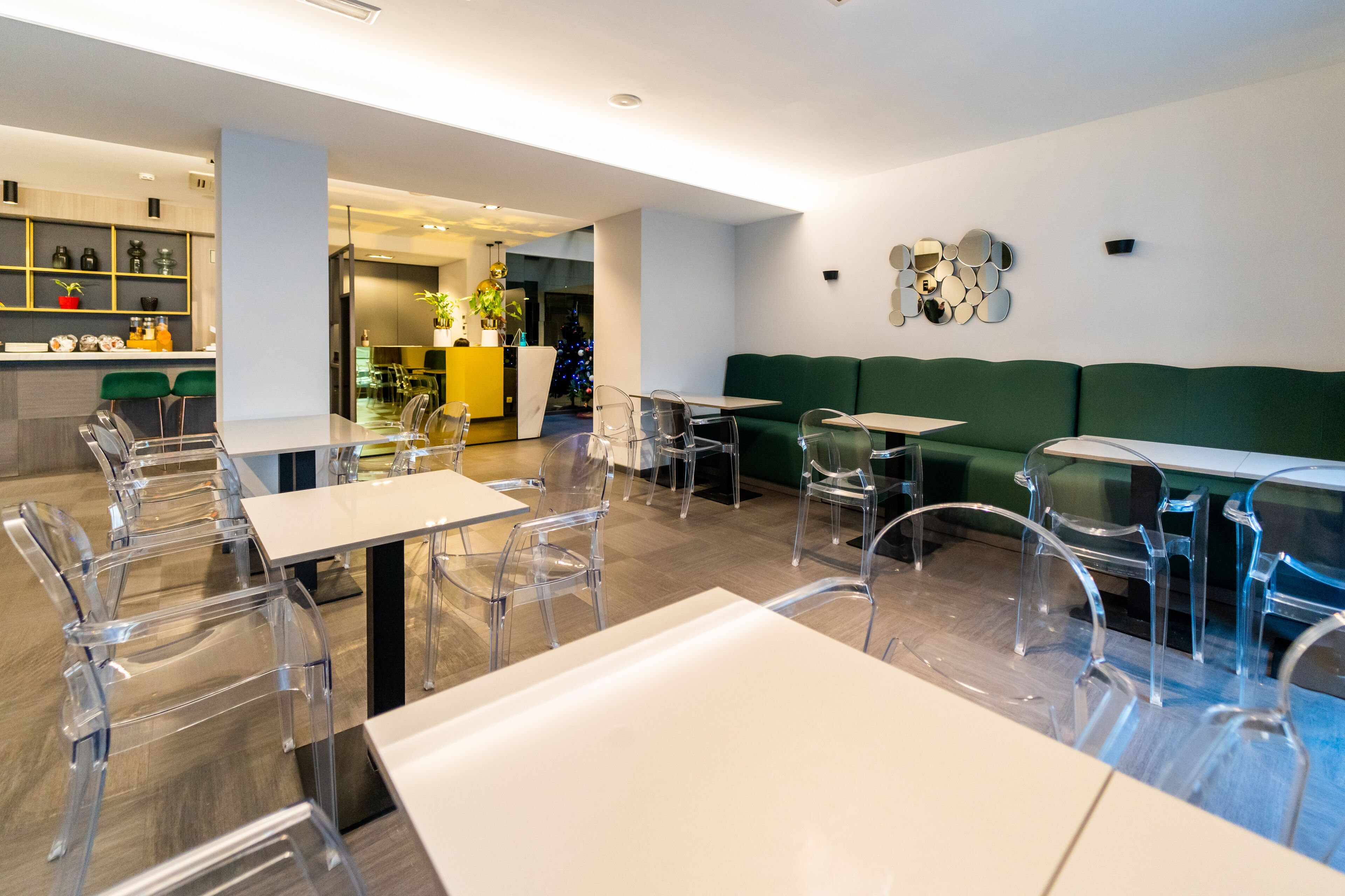 A modern restaurant with clear chairs and tables, a green sofa, and a bar area with shelves and decorative items.