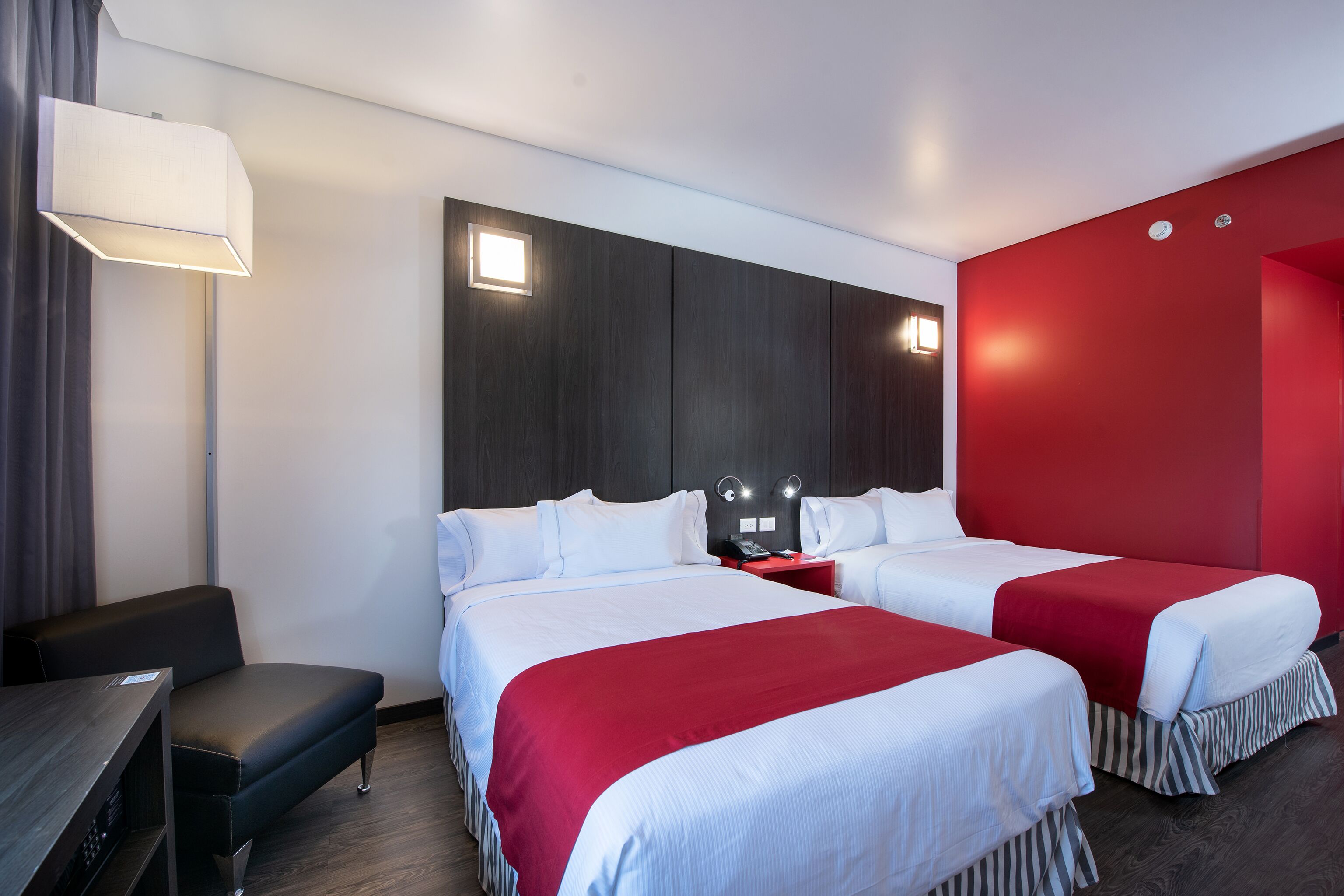 Habitación de hotel con dos camas, un escritorio, una silla, una lámpara y una pared de acento roja.