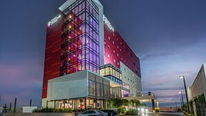 Un hotel de varios pisos con fachada moderna de vidrio, señalización de Encore by Hilton y vista al océano.