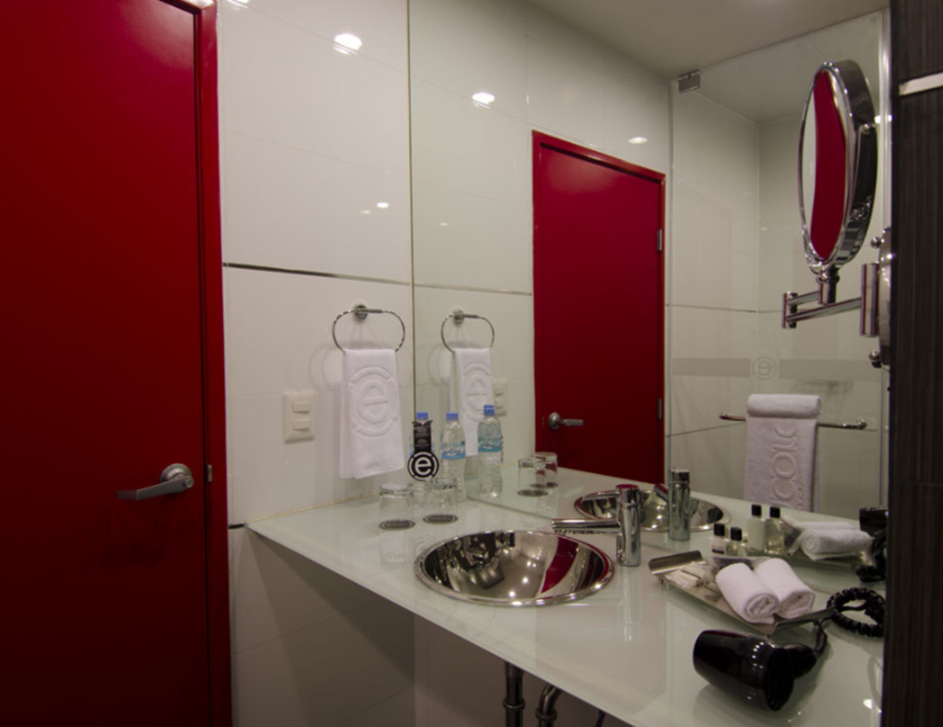 Un baño moderno con un espejo grande, un lavamanos y una puerta roja.