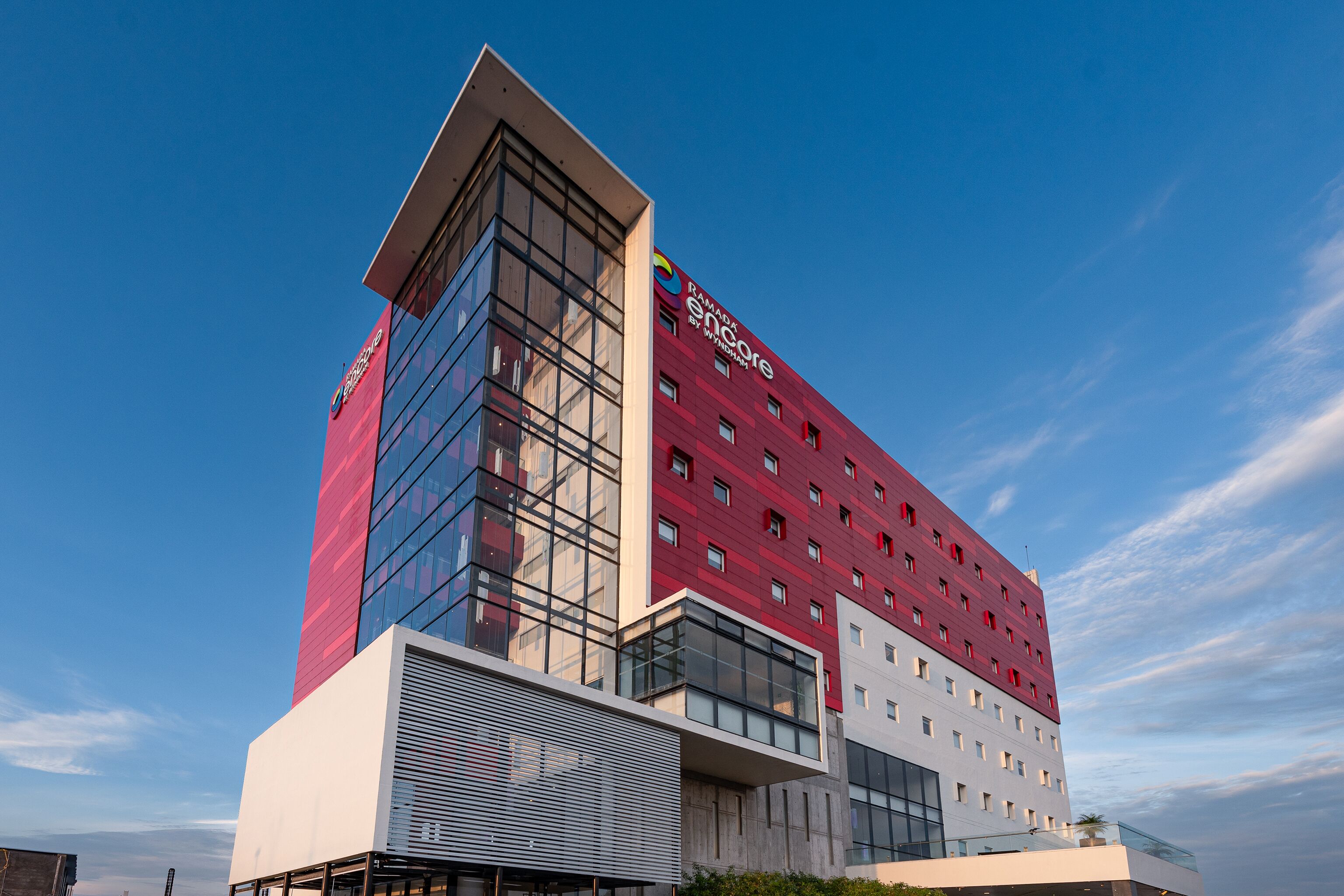 Un hotel moderno con fachada roja y blanca, grandes ventanales y un logotipo destacado.
