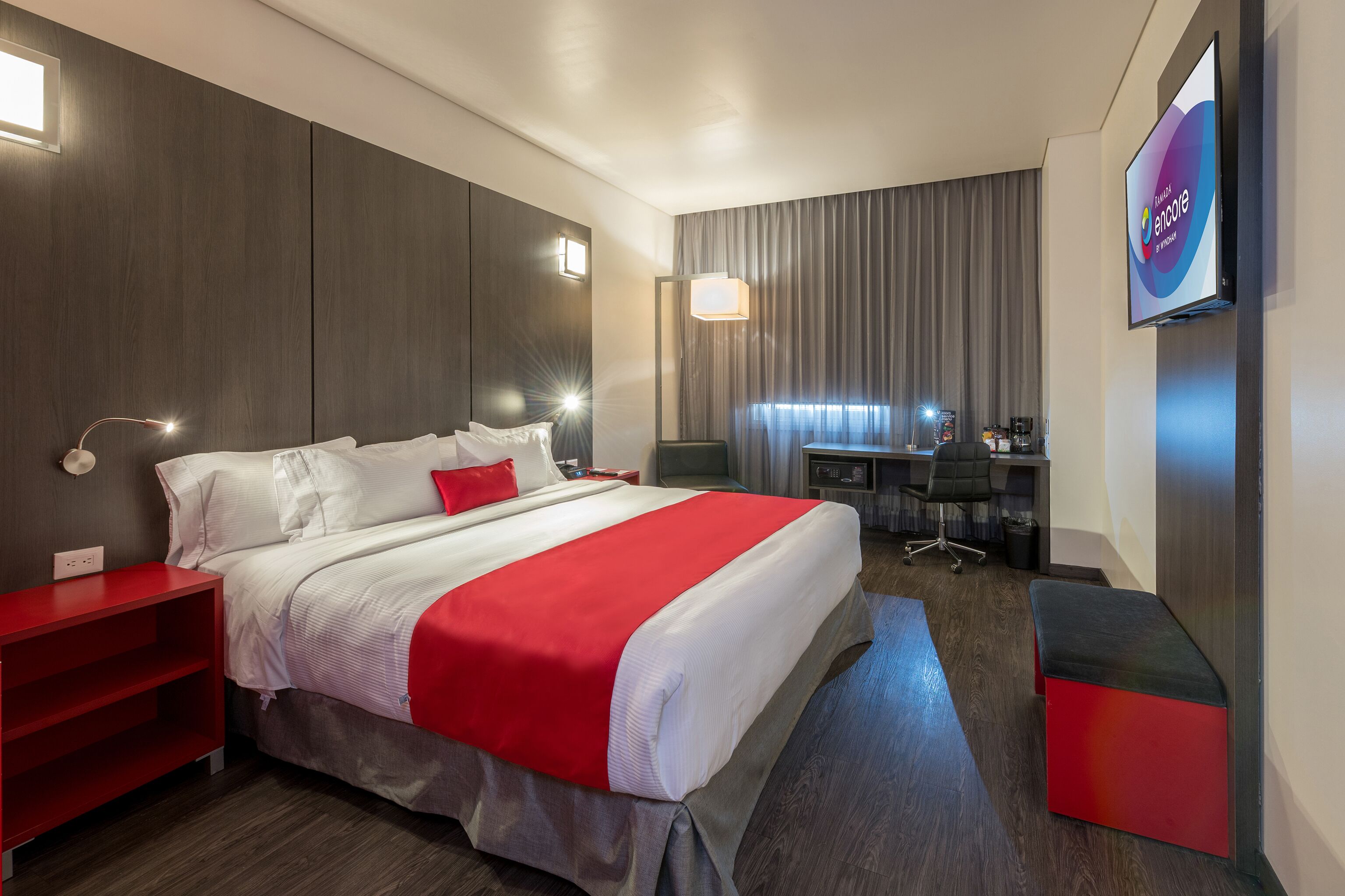 A modern hotel room with a large bed, a desk, and a TV.