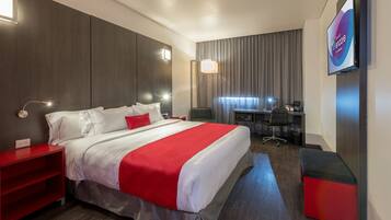 A modern hotel room with a large bed, a desk, and a TV.