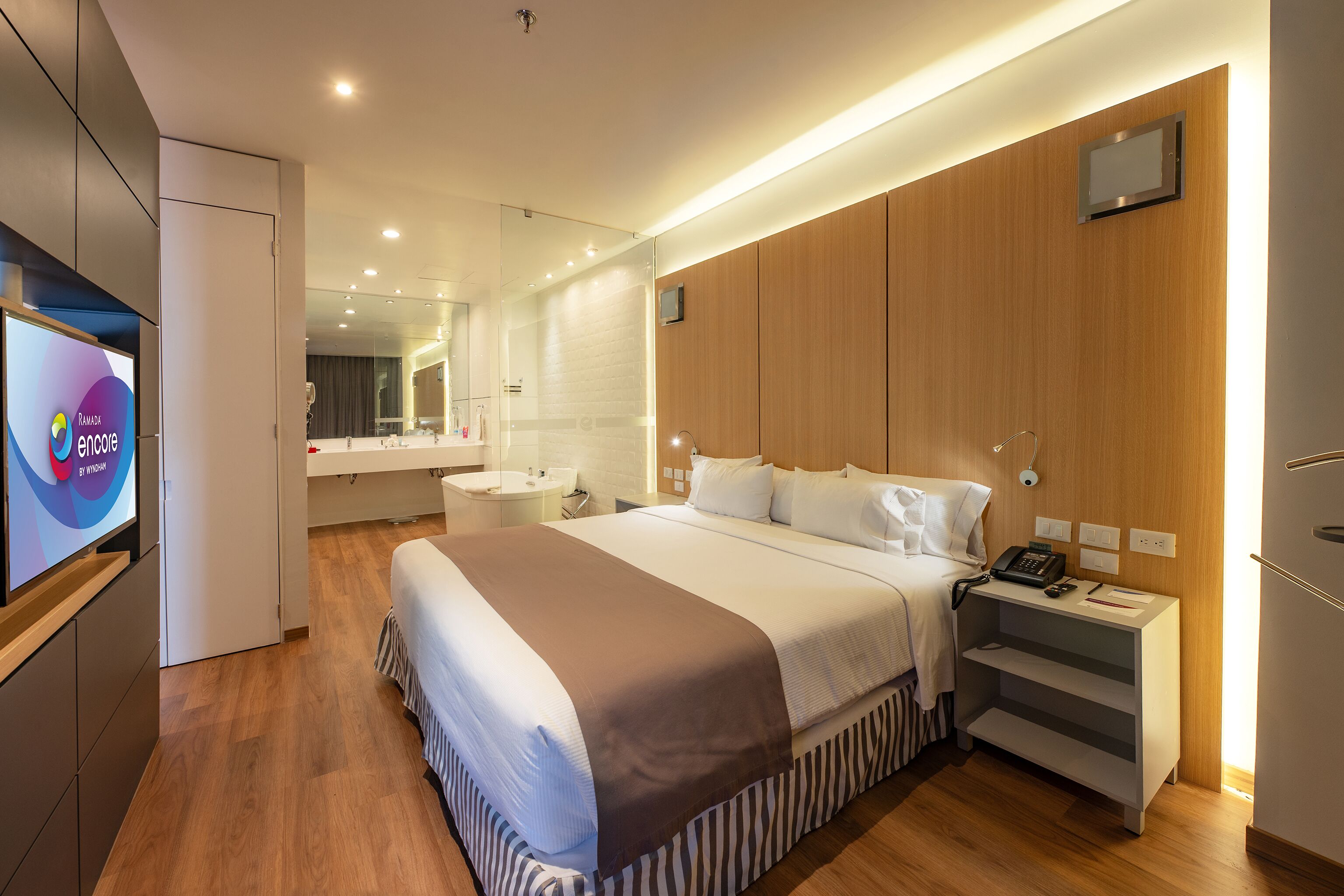 Una habitación de hotel moderna con una cama grande, una mesita de noche y un televisor que muestra el logotipo de Ramada.