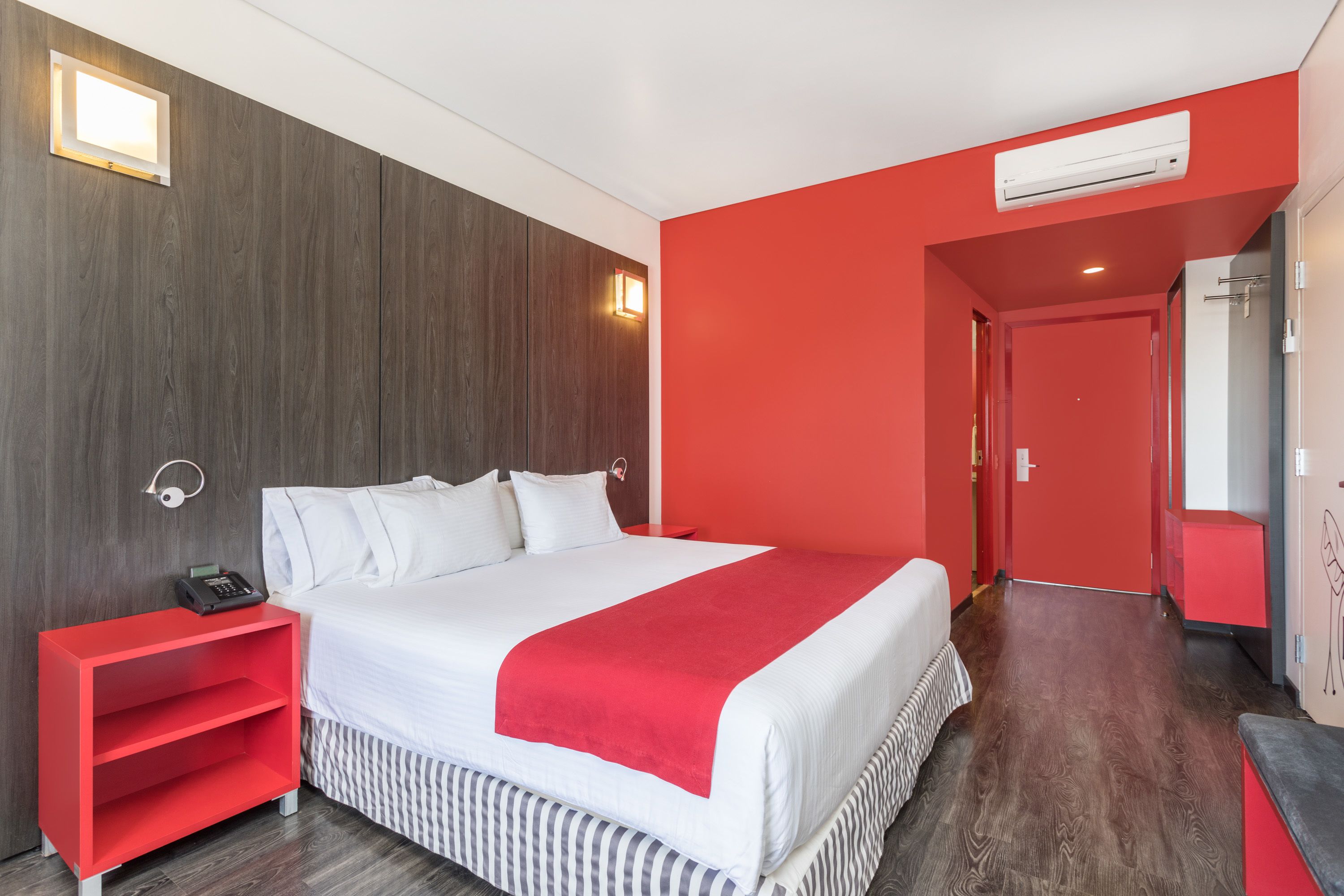 Habitación de hotel con una cama grande, una mesita de noche roja, una pared roja y suelo de madera.