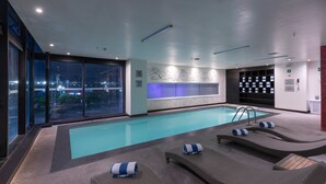 Una piscina interior moderna con sillones de descanso y vistas a la ciudad.