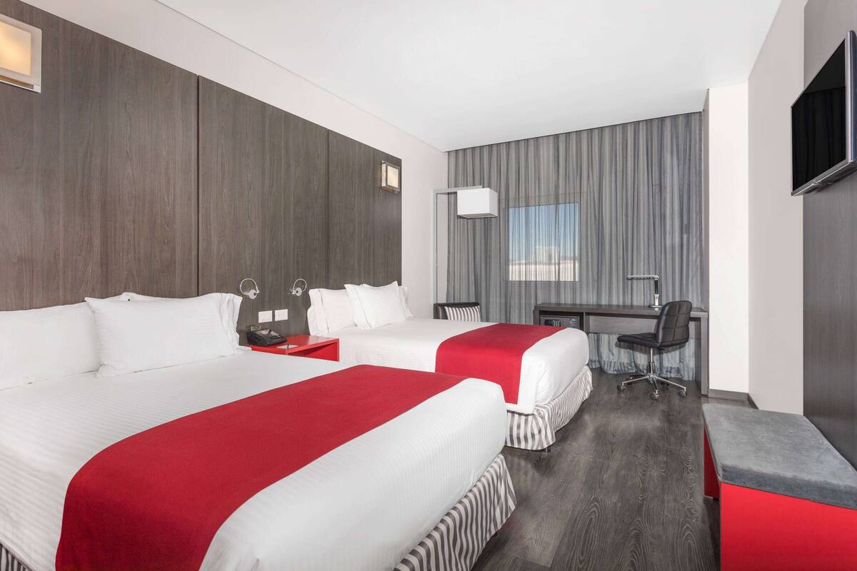 A hotel room with two beds, a desk, and a TV.