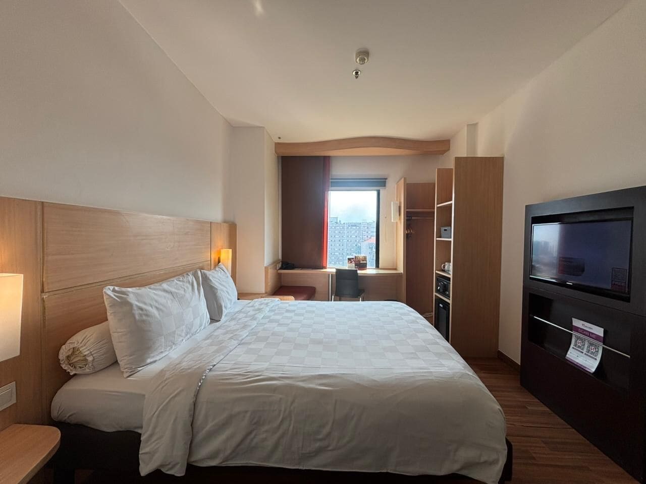 Habitación de hotel con cama, escritorio, televisor y vistas a la ciudad.