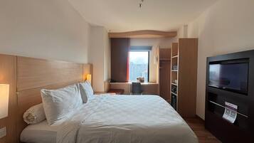 Habitación de hotel con cama, escritorio, televisor y vistas a la ciudad.