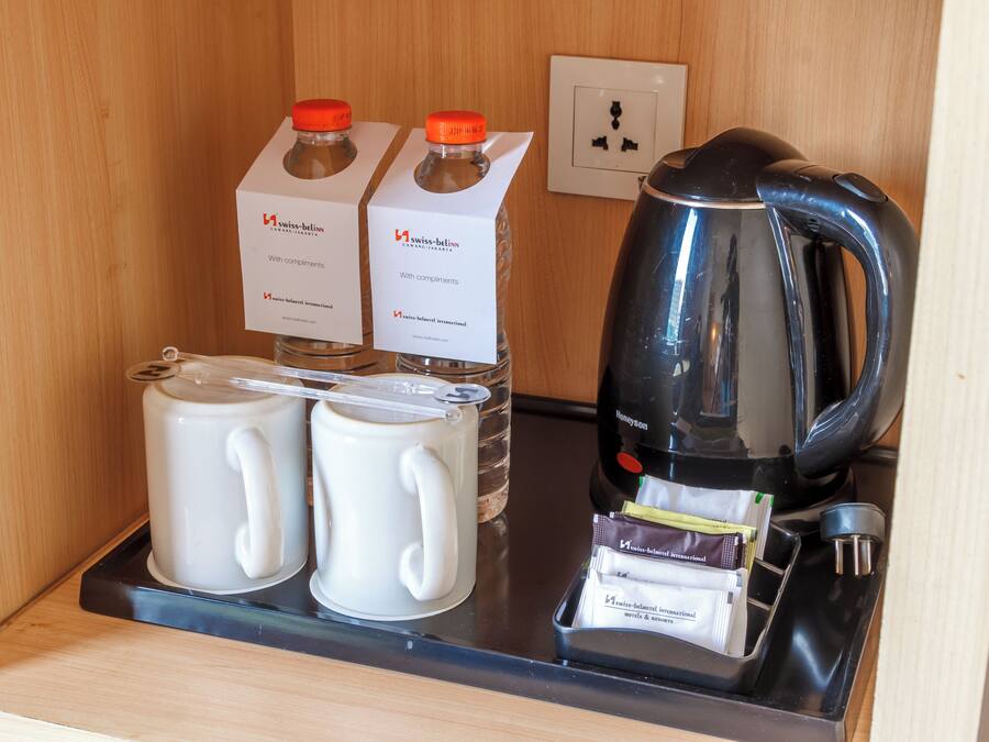 A hotel minibar with two milk cartons, two white mugs, a black coffee maker, and a tray with various items.