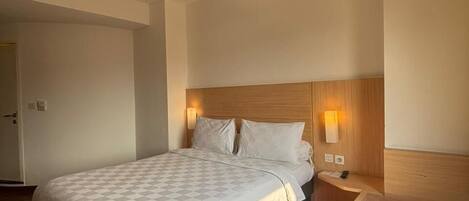A hotel room with a large bed, bedside tables, a chair, and a wooden floor.