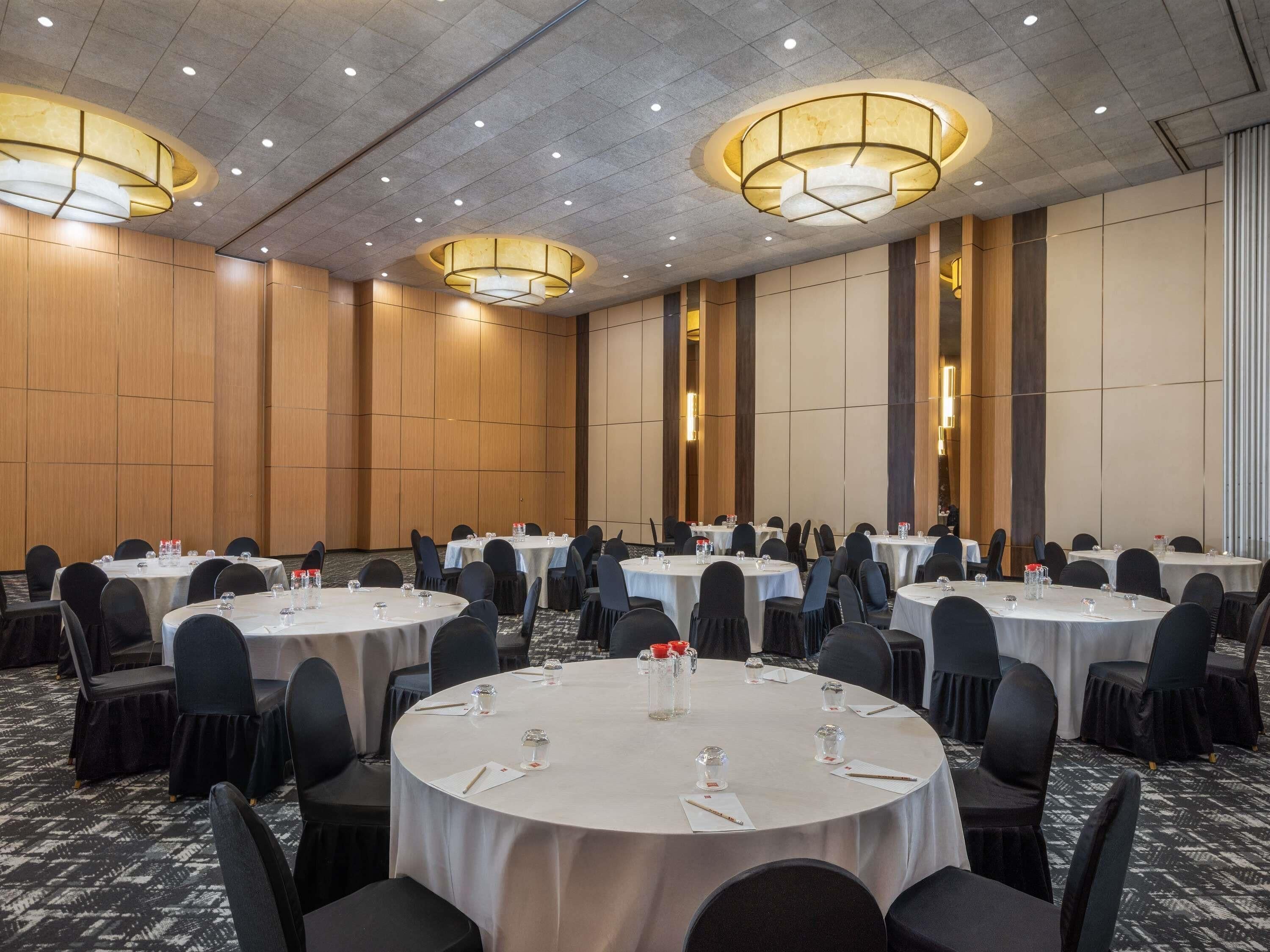 Un salón de conferencias con mesas redondas, sillas negras y un techo alto con iluminación empotrada.