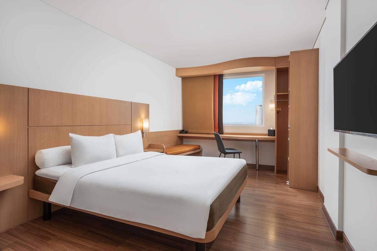A modern hotel room with a large bed, a desk, and a TV.
