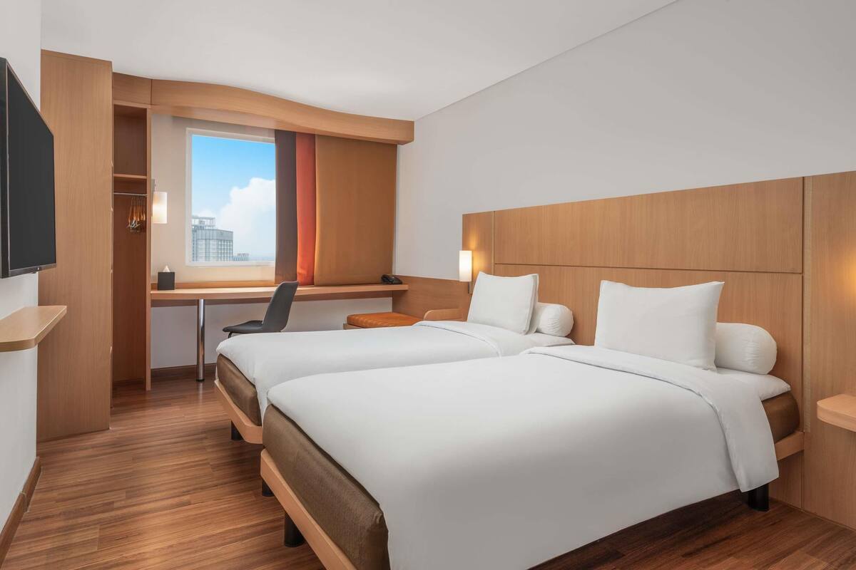A hotel room with two beds, a desk, a chair, and a TV.
