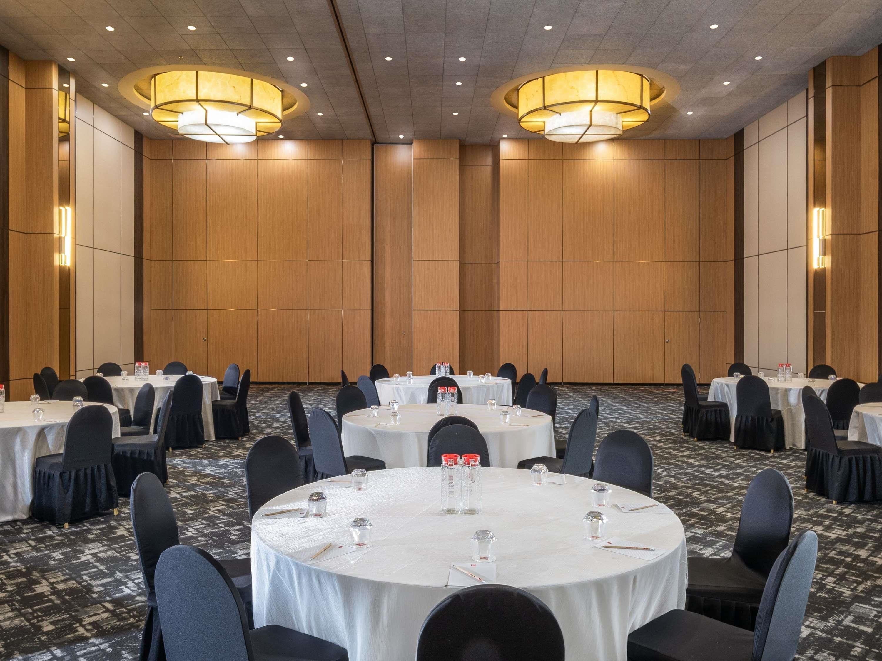 A conference room with round tables, black chairs, and wooden panel walls.