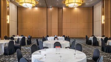 Een vergaderzaal met ronde tafels, zwarte stoelen en houten paneelwanden.