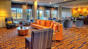 A hotel lobby with a large orange sofa, a grey armchair, a coffee table, and a reception desk. - Courtyard San Marcos (San Marcos)