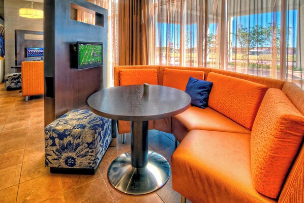 A modern lobby with a round table, orange sofa, and a flat-screen TV mounted on the wall. - Courtyard San Marcos (San Marcos)