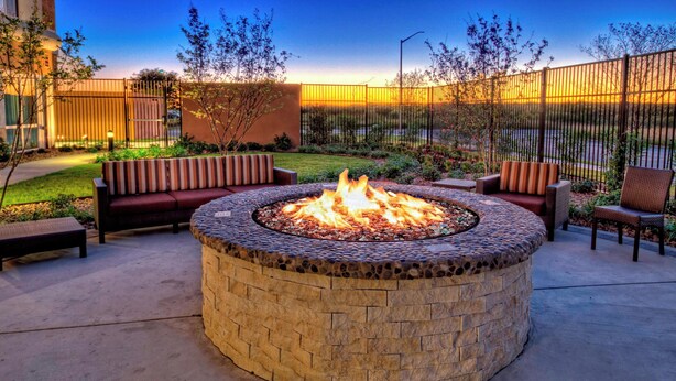 A circular stone fire pit with seating around it, set in a courtyard with a fence and trees. - Courtyard San Marcos (San Marcos)