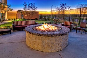 A circular stone fire pit with seating around it, set in a courtyard with a fence and trees. - Courtyard San Marcos (San Marcos)
