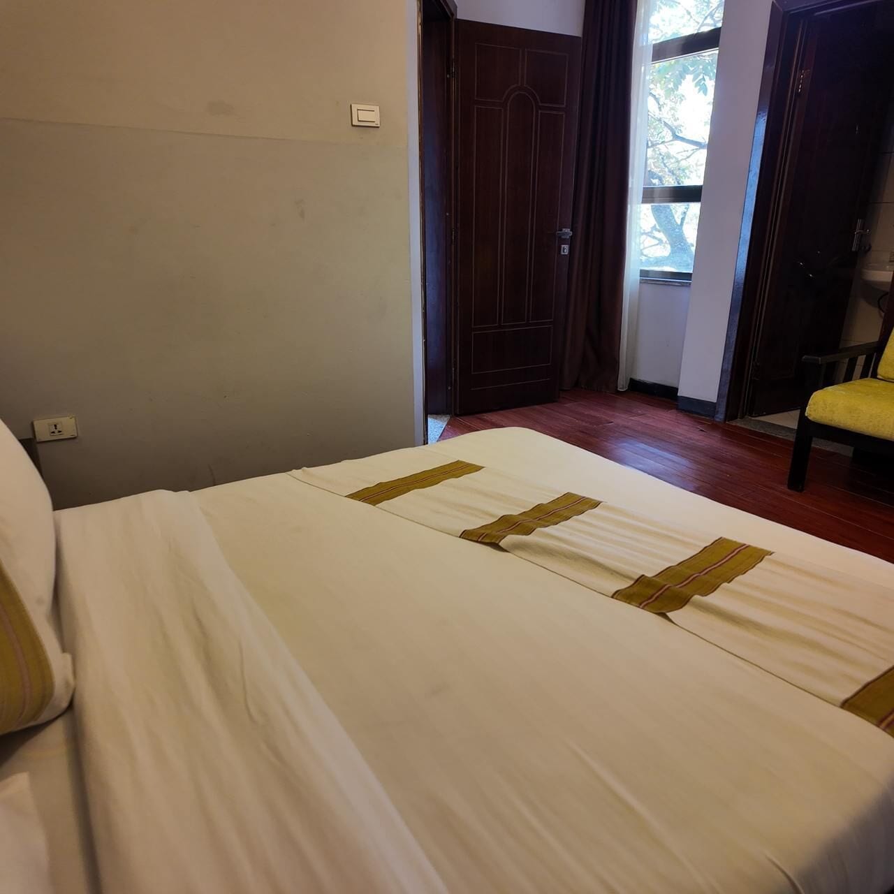 A hotel room with a bed, a wooden floor, a door, and a chair.