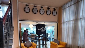 A coffee shop interior with yellow sofas, a staircase, and multiple clocks on the wall. - Hotel Lobelia (Addis Ababa)