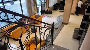 A hotel lobby with a staircase, a reception desk, and a seating area with yellow sofas. - Hotel Lobelia (Addis Ababa)