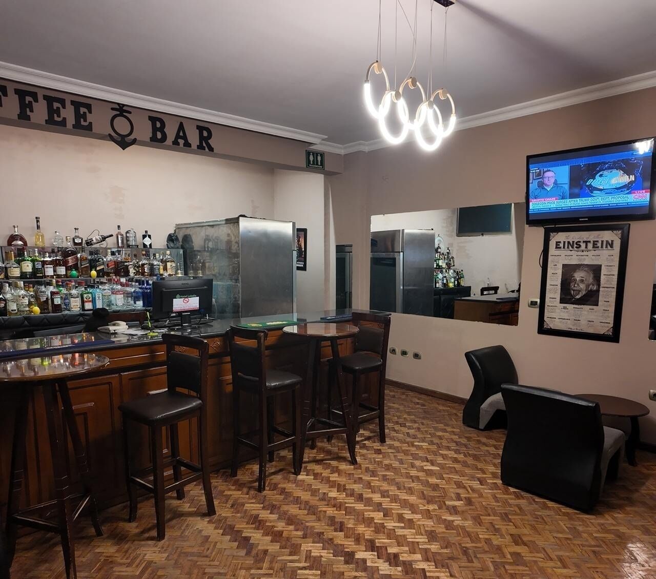 Una zona de bar con suelo de madera en espiga, una barra con taburetes, un televisor montado en la pared y un cartel de Einstein.