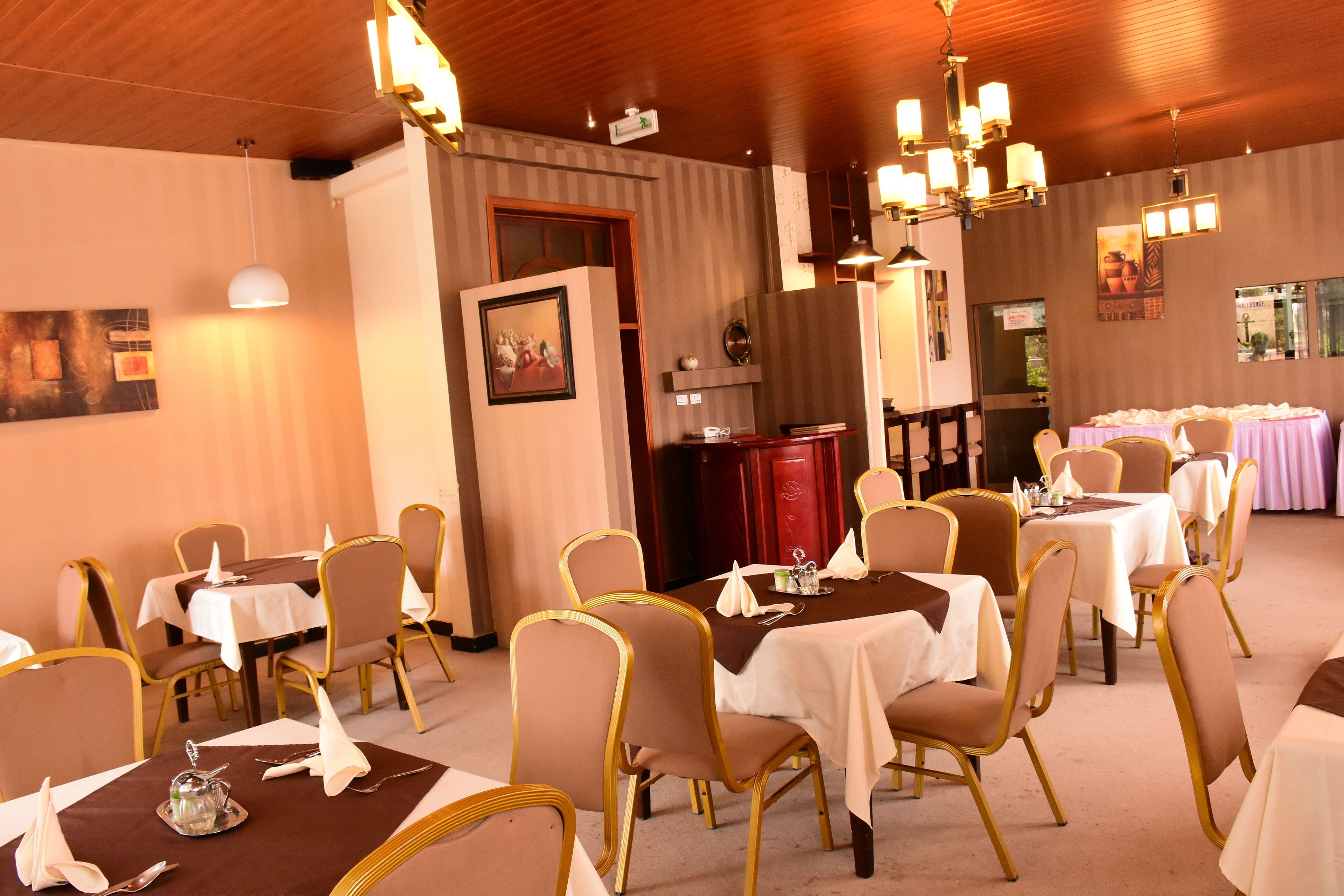 A dining area with multiple tables and chairs, a wooden ceiling, and wall-mounted lighting fixtures.