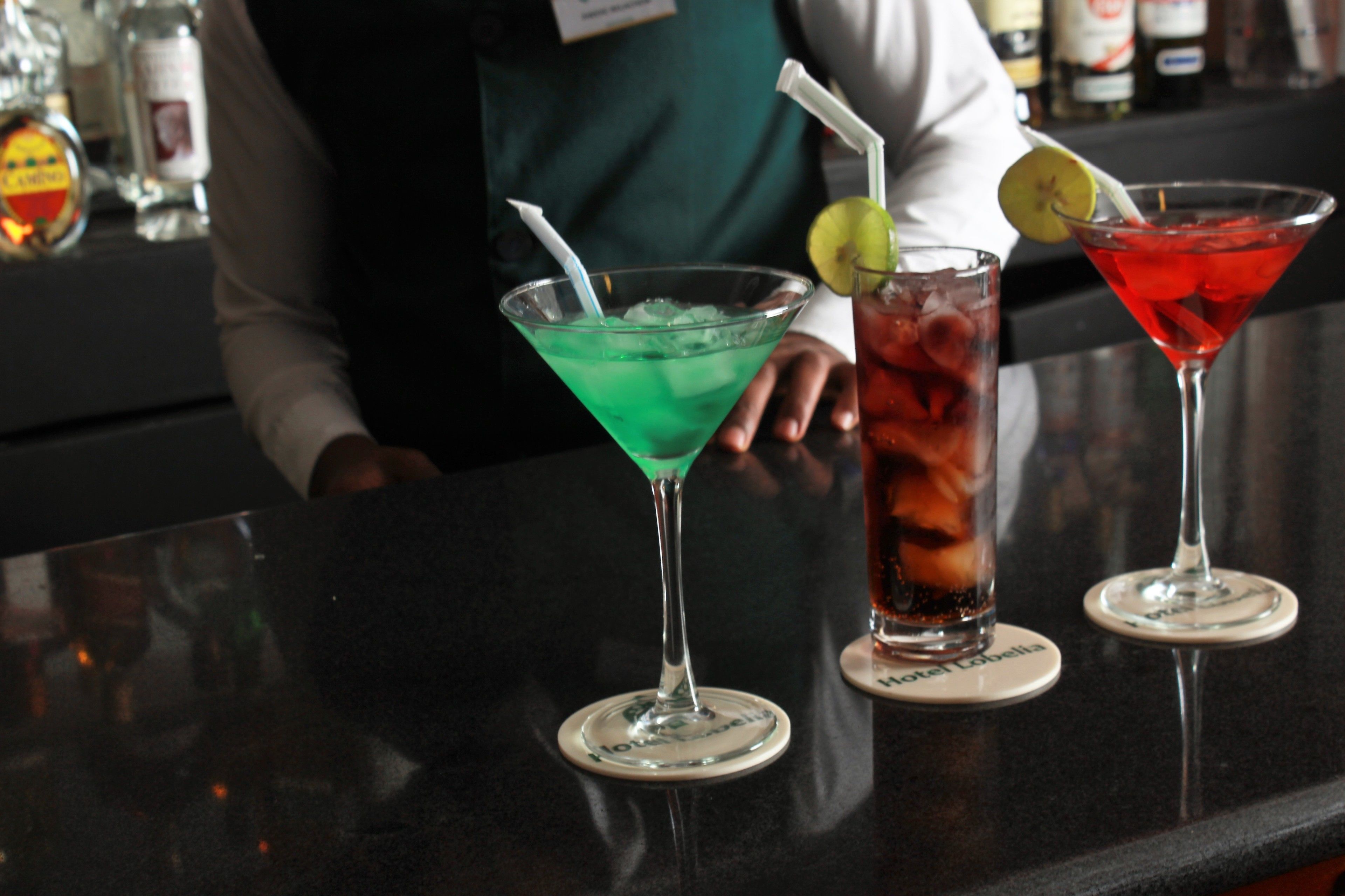 Three cocktails on a bar counter with a bartender in the background.