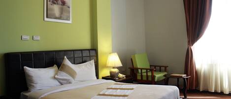 A hotel room with a bed, a nightstand with a lamp, a chair, and a painting on the wall.