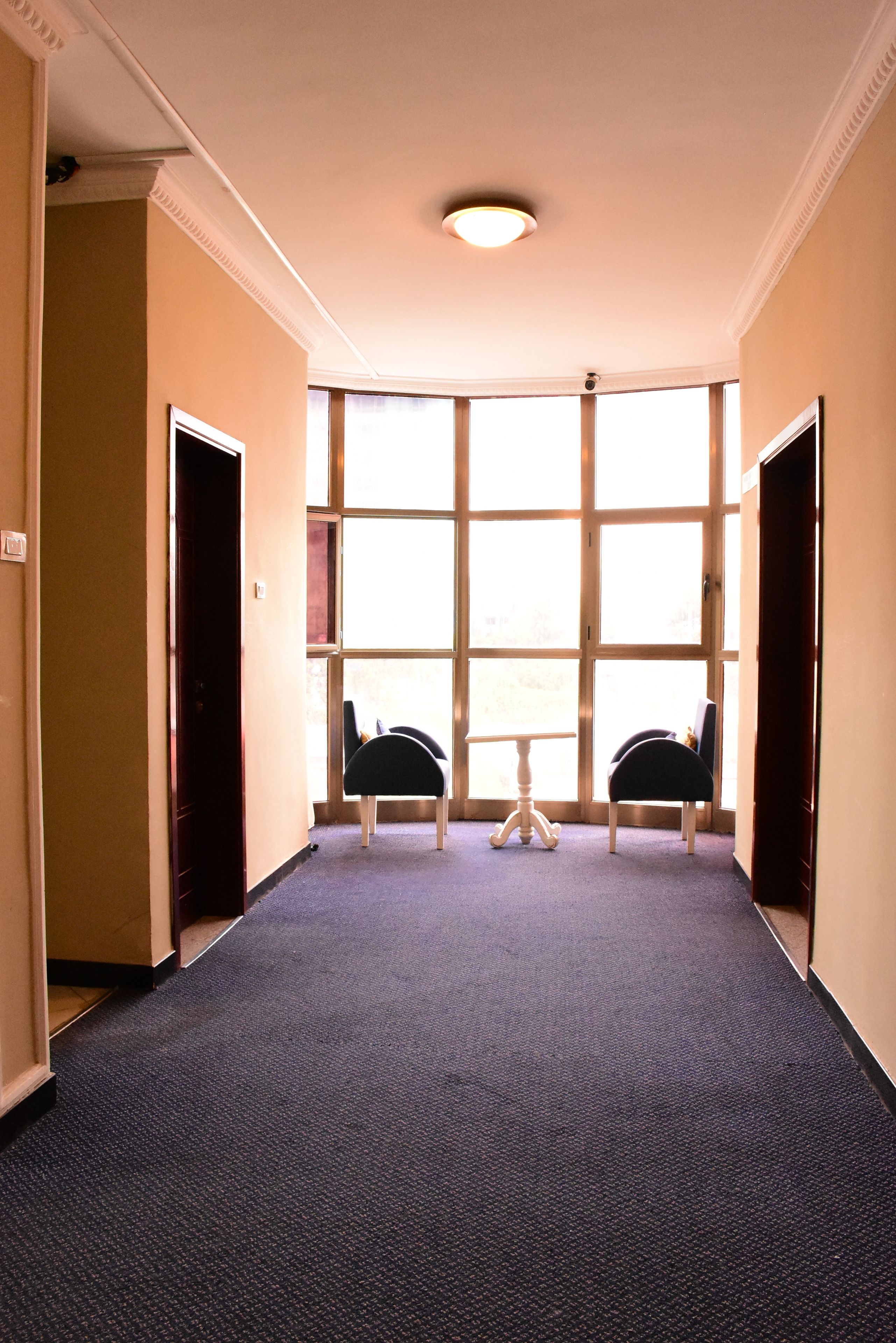 Un couloir avec deux chaises, une petite table et de grandes fenêtres.