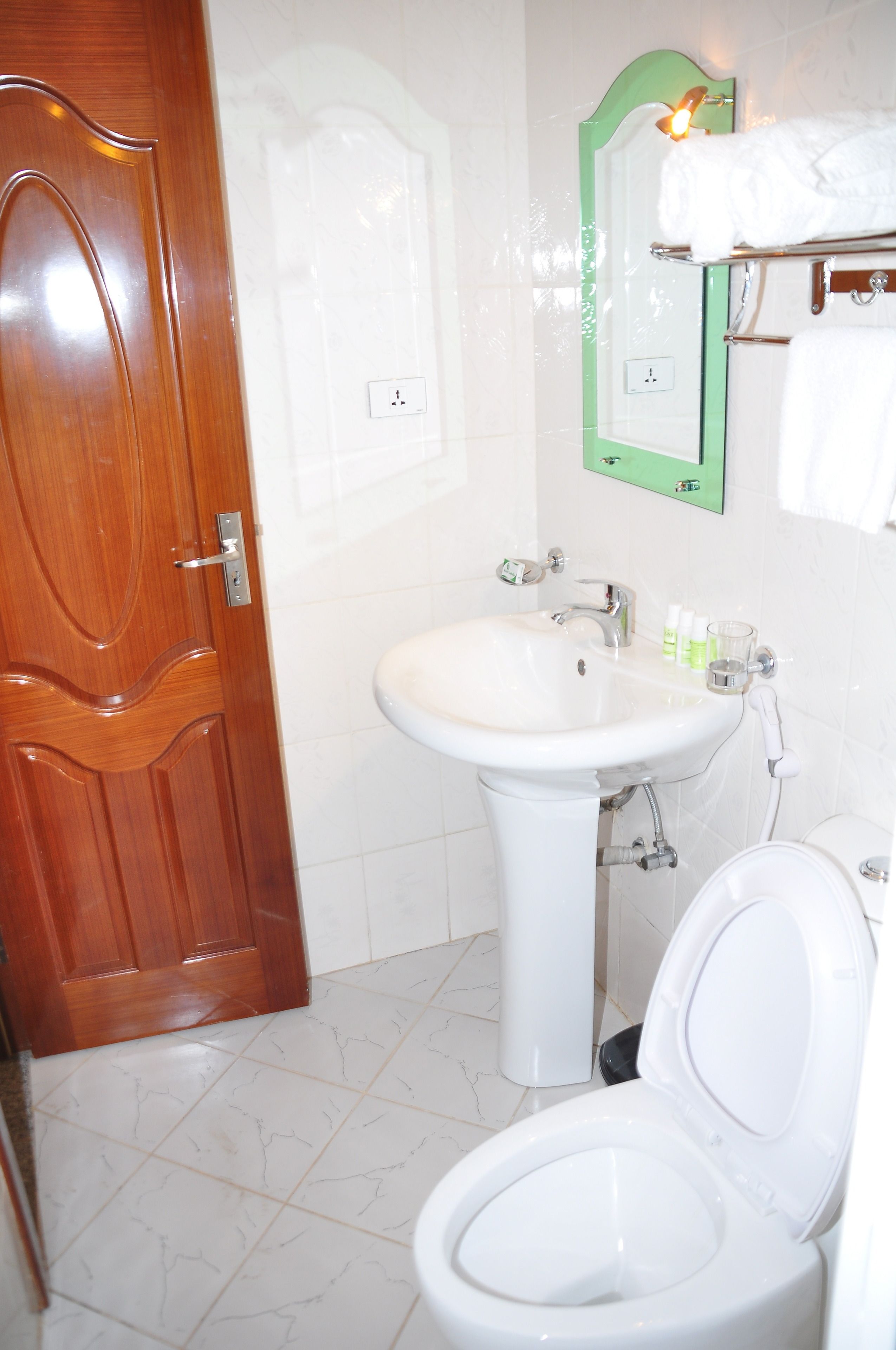 Un baño con puerta de madera, un lavamanos blanco, un inodoro y un espejo con marco verde.