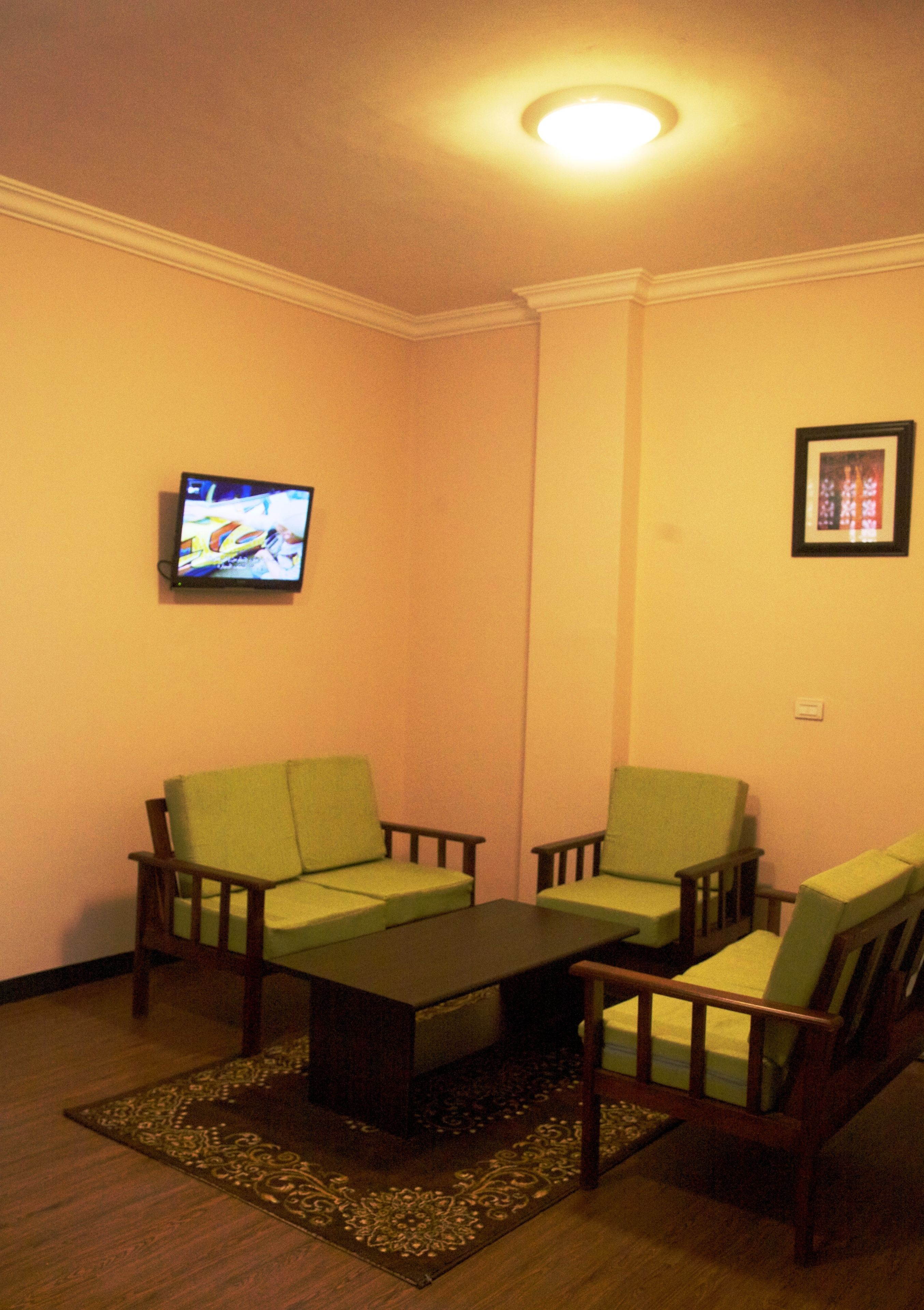 Un salón con dos sillones verdes, una mesa de centro de madera, un televisor en la pared y un cuadro enmarcado.