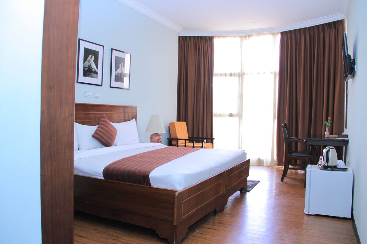 A hotel room with a large bed, a desk, a chair, and a window with curtains.