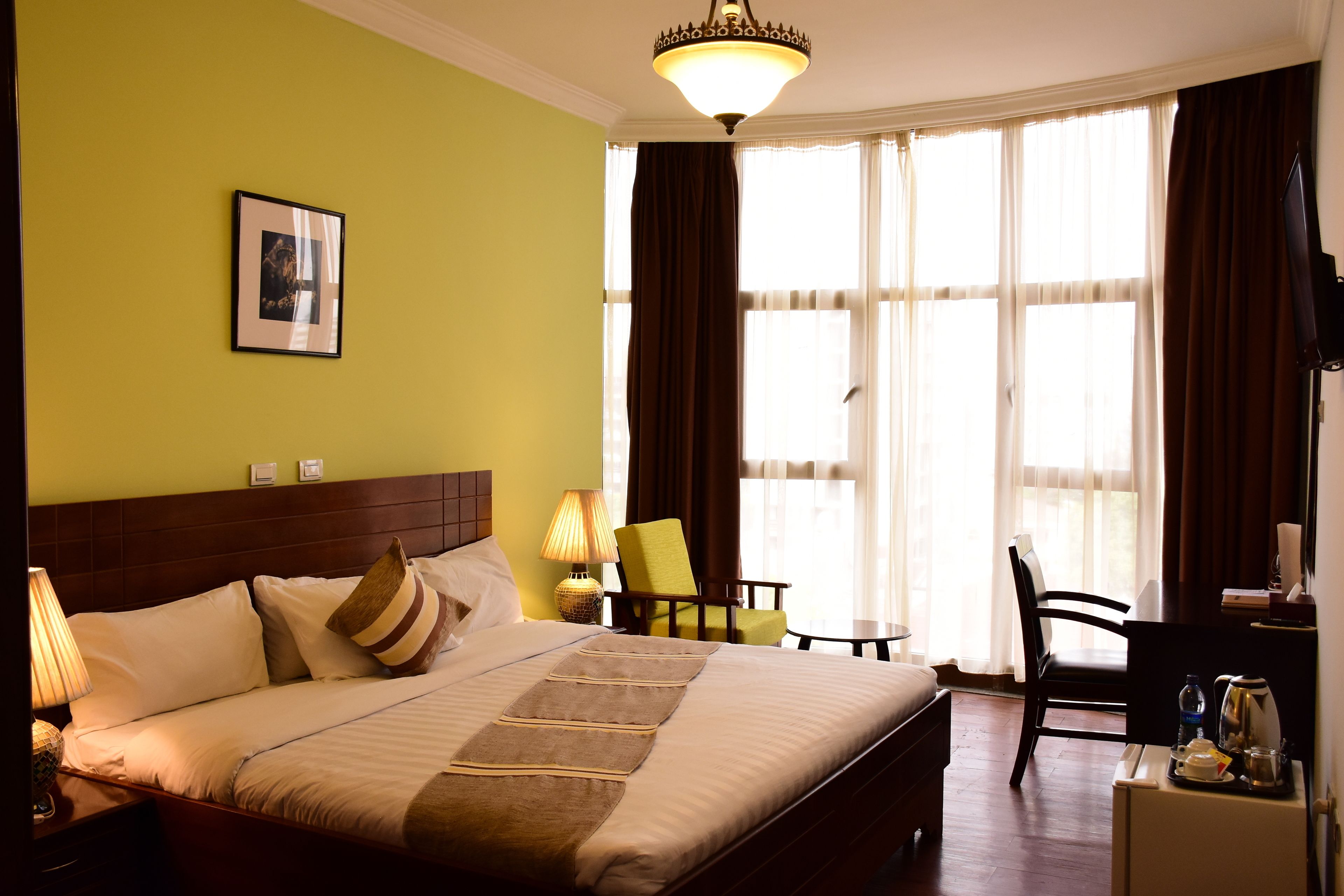 A hotel room with a bed, a desk, a chair, a lamp, and a picture on the wall.