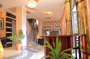 Vestíbulo de hotel con una barra de café, una escalera y plantas en macetas.