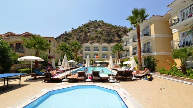 A pool area with lounge chairs and umbrellas, surrounded by buildings with balconies and a mountain in the background.