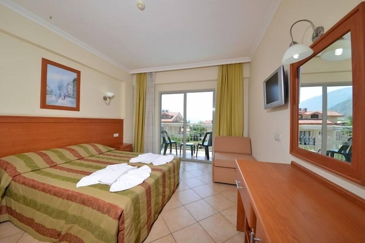 Habitación de hotel con cama, escritorio, silla, televisor y balcón con vistas.