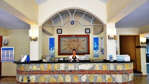A reception area with a stone counter, a receptionist, a large sun mural, and a clock on the wall.