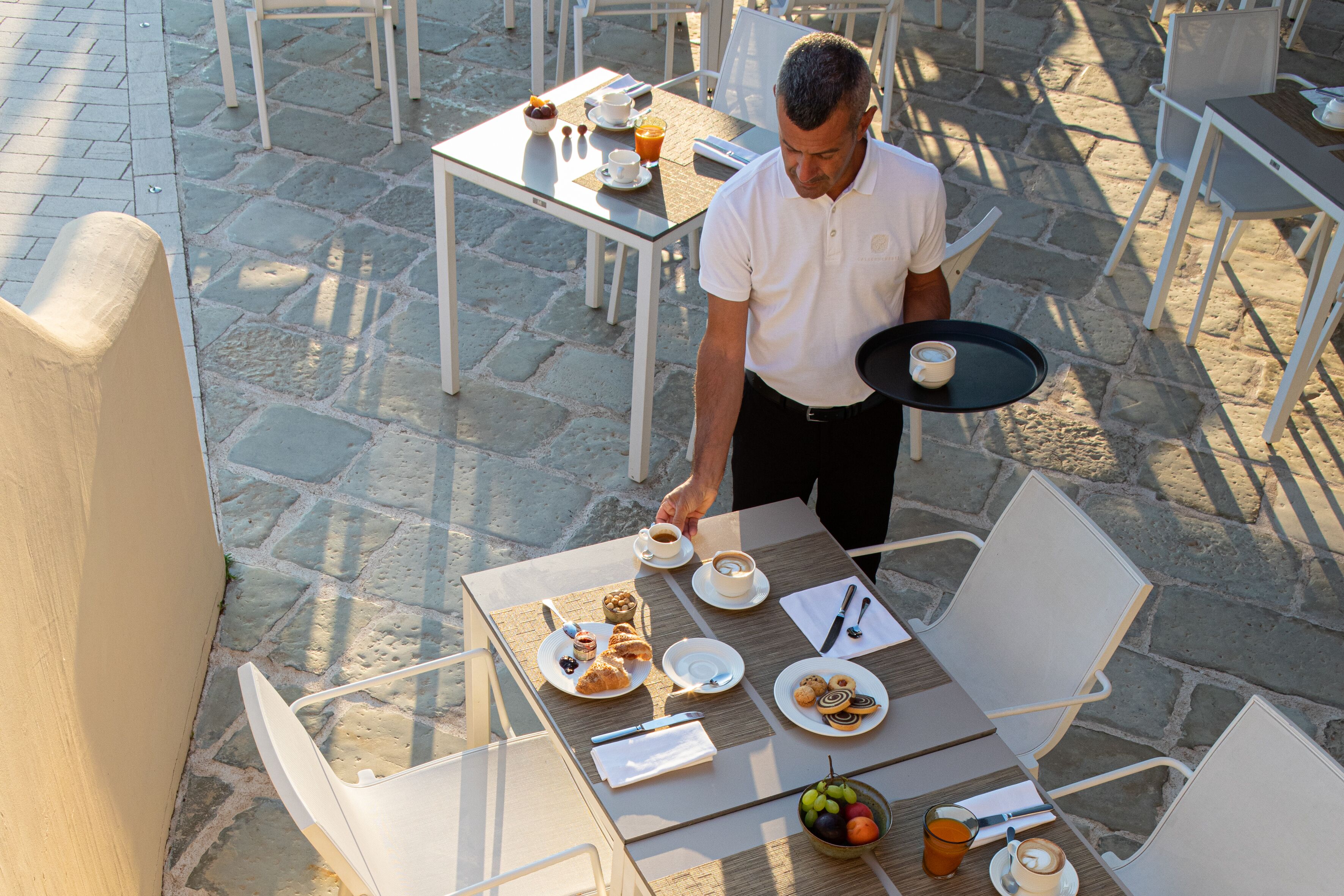 Una mesa preparada con alimentos para el desayuno, incluyendo pasteles y fruta, en un café al aire libre.