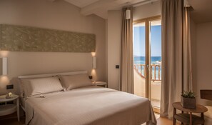 A bedroom with a large bed, a nightstand, a bedside table, a potted plant, and a view of the sea through a sliding glass door. - Cala Cuncheddi - VRetreats (Olbia)