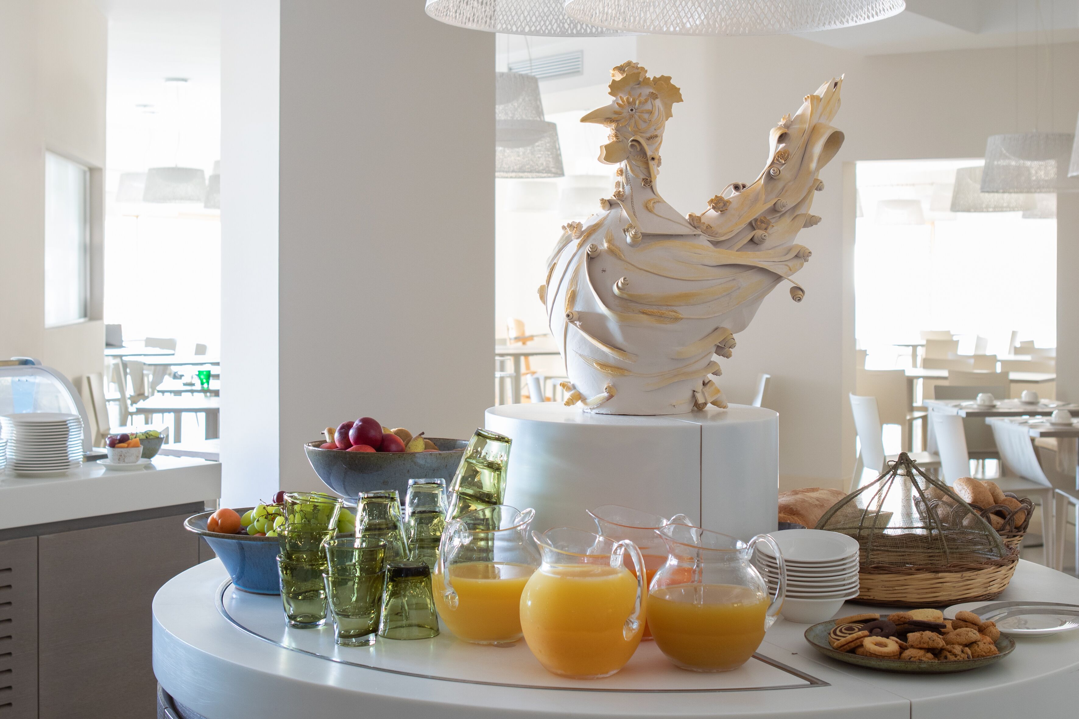 A breakfast buffet with a decorative rooster centerpiece, fruit bowl, and various beverages.