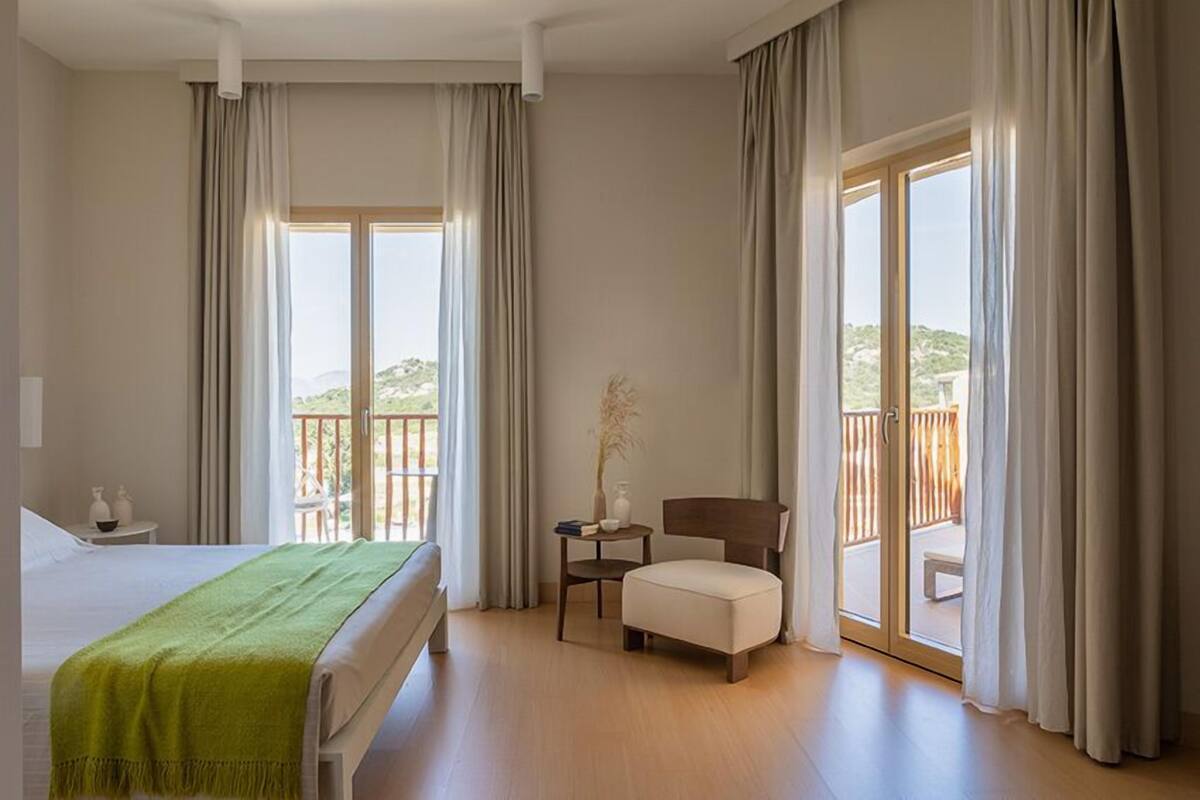 A hotel room with a bed, a chair, a small table, and a balcony with a view.